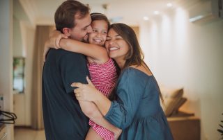 Parents and daughter hugging and smiling in the living room.