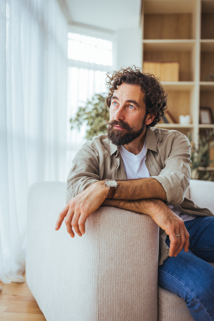 Thoughtful Bearded Man Sitting On Sofa In Bright Modern Living Room Looking Out Window Men After Divorce: What Do You Do When Life Feels Empty?